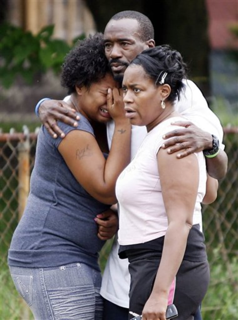 Michael Harris consoles family and friends outside a home in Indianapolis after a masked man armed with an assault-style rifle fired dozens of shots on a birthday party early Tuesday, killing two people and wounding six before fleeing, police said. 